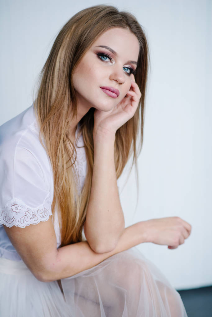 Όμορφη νεαρή γυναίκα με μακιγιάζ σε λευκό φόρεμα που θέτουν σε στούντιο - Φωτογραφία, εικόνα