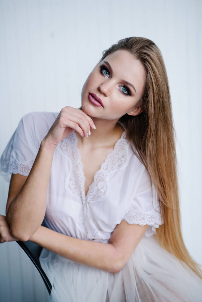 Mooie jonge vrouw met make-up in witte jurk poseren in studio - Foto, afbeelding