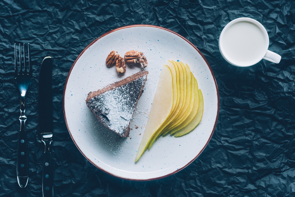 pohled shora dort broušená hruška na talíř a hrnek mléka na tmavý stůl - Fotografie, Obrázek