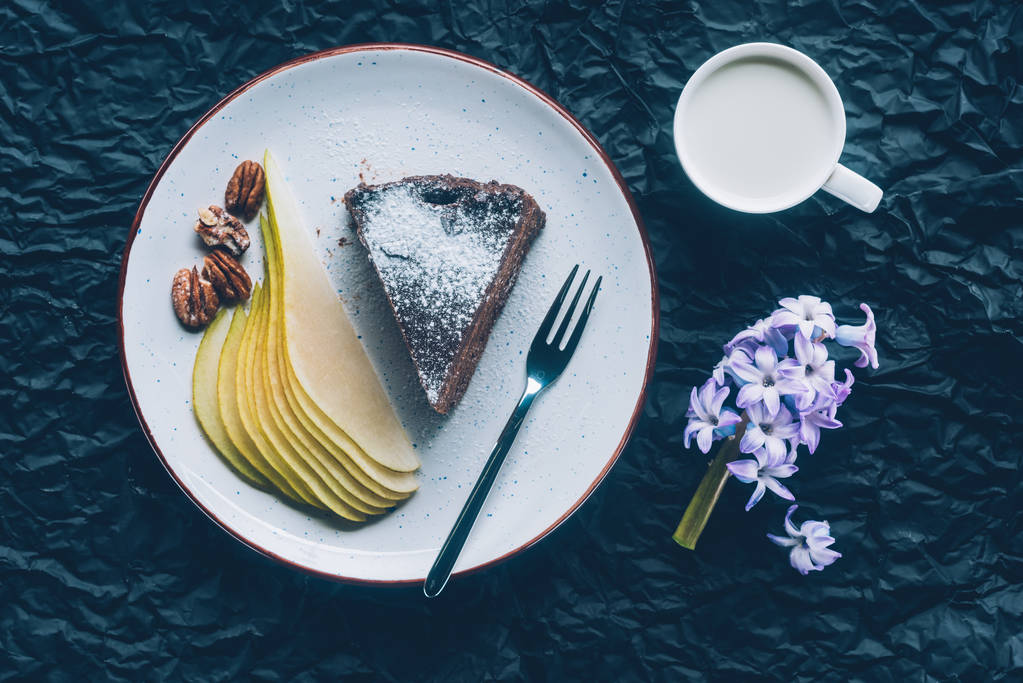 pohled shora dort broušená hruška na talíř a hrnek mléka na tmavý stůl - Fotografie, Obrázek