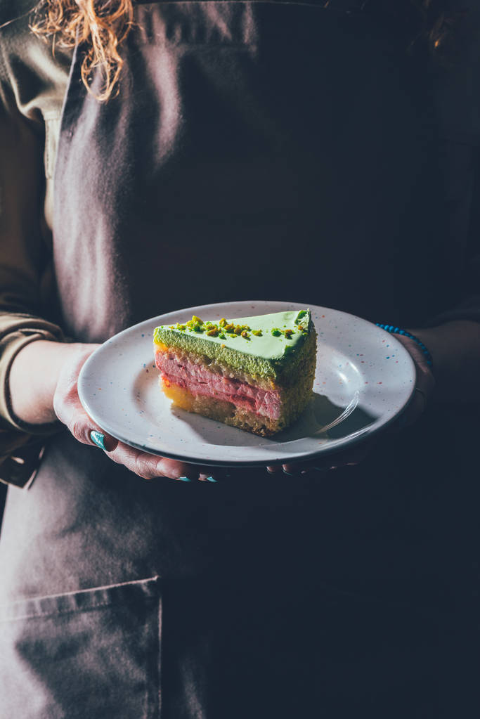 κλείνω πάνω θέα της γυναίκας κρατώντας κομμάτι σπιτικό κέικ στο πιάτο στα χέρια - Φωτογραφία, εικόνα