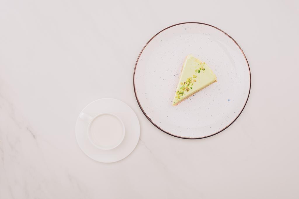 top view of piece of cake on plate and cup of milk on white surface - Photo, Image