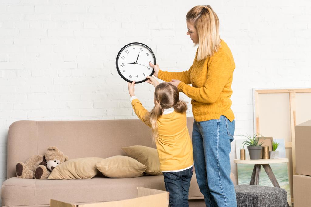 beautiful mother and daughter hanging clock on wall during relocation   - Photo, Image