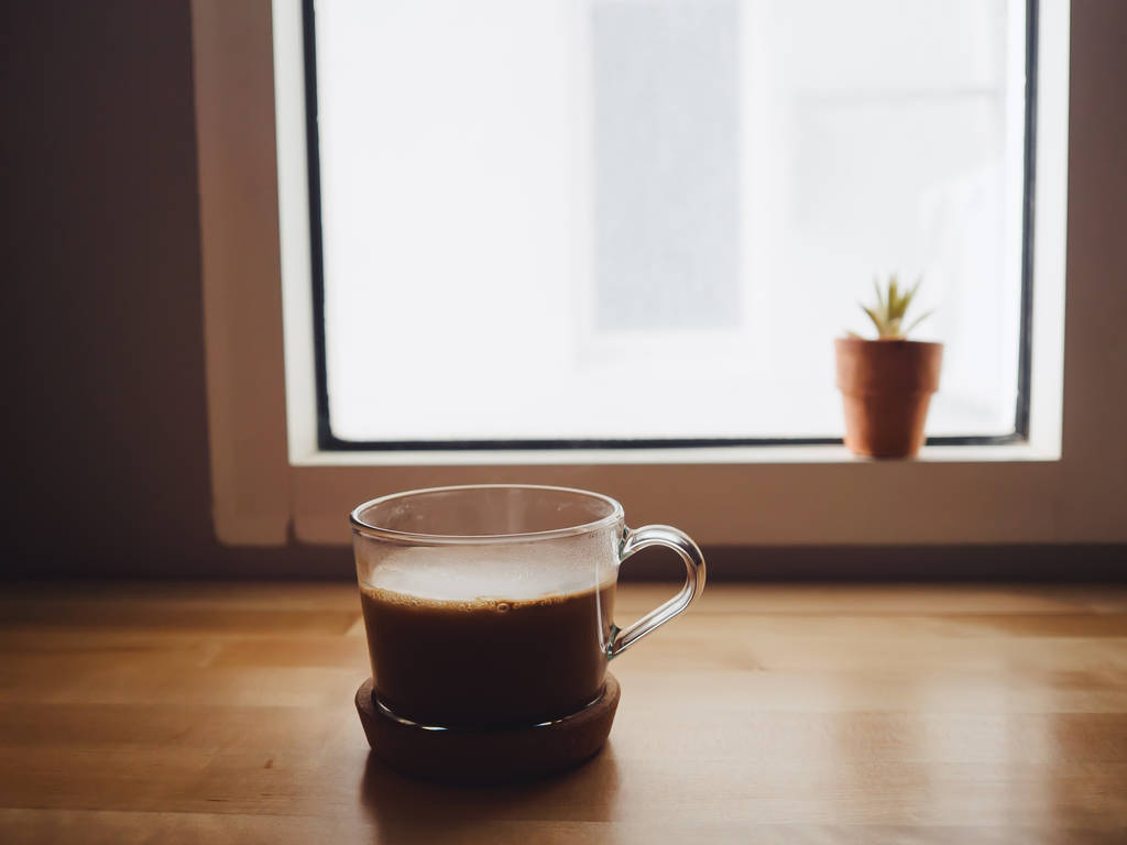 Taza de café caliente en la mesa en condiciones de poca luz junto a la ventana
 - Foto, Imagen
