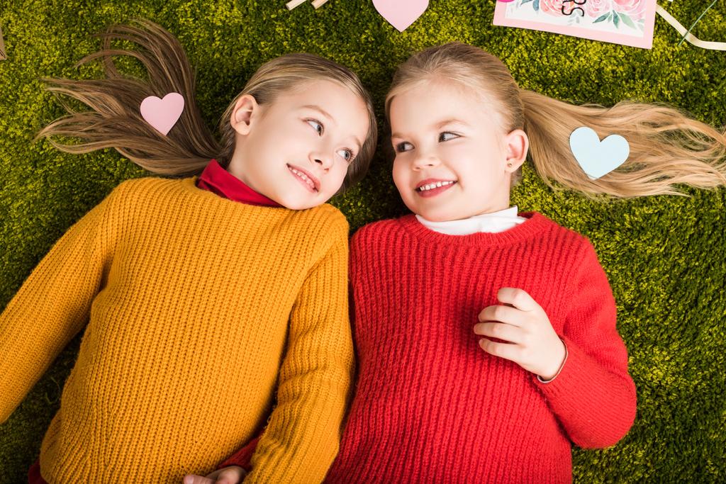 Draufsicht auf entzückende kleine Schwestern, die auf Teppich liegen, umgeben von Herzen - Foto, Bild
