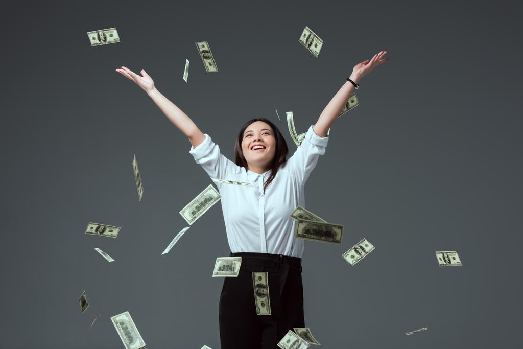 glückliche junge Asiatin wirft Dollarnoten isoliert auf grau - Foto, Bild