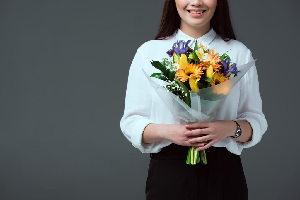 abgeschnittene Aufnahme einer lächelnden jungen Frau mit einem Blumenstrauß isoliert auf grau - Foto, Bild