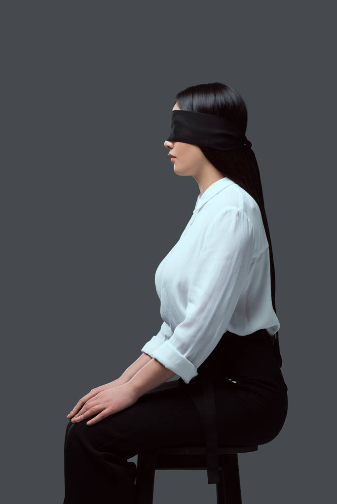 side view of young blindfolded woman sitting on chair isolated on grey - Photo, Image