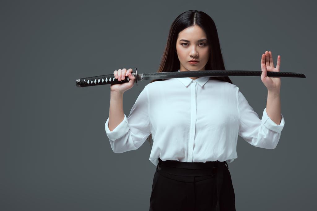 beautiful asian girl holding katana sword and looking at camera isolated on grey  - Photo, Image