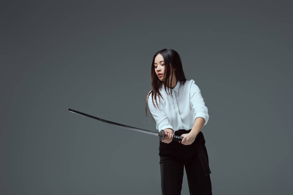 красивая азиатская девушка держит катану меч изолирован на серый
 - Фото, изображение