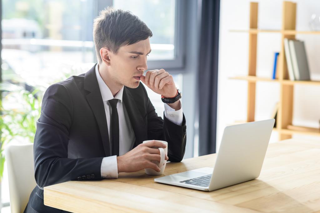 Молодой бизнесмен смотрит на экран ноутбука в современном офисе
   - Фото, изображение