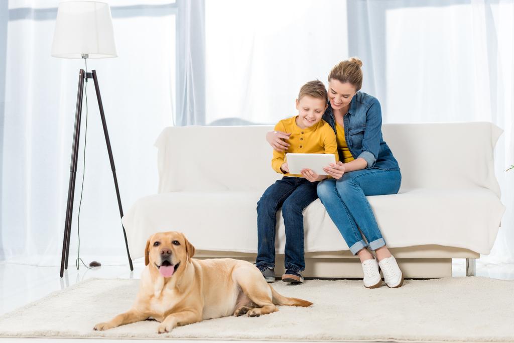 mother and son using tablet together with adorable dog lying on floor on foreground - Photo, Image