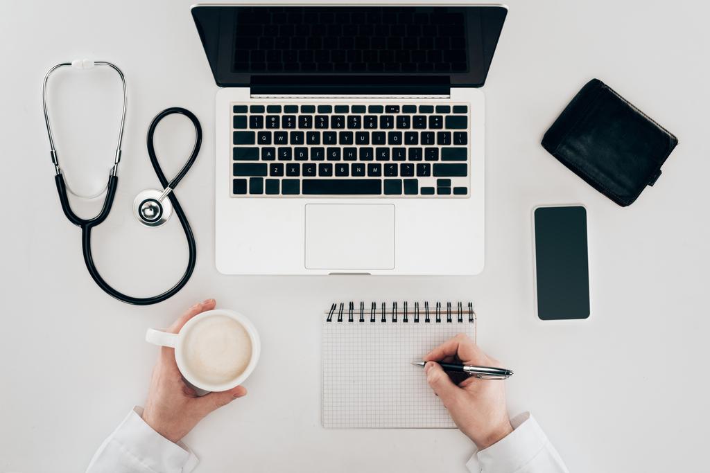 osittainen näkymä lääkärin työpaikalla kannettavan tietokoneen, stetoskoopin ja kupin kahvia
 - Valokuva, kuva