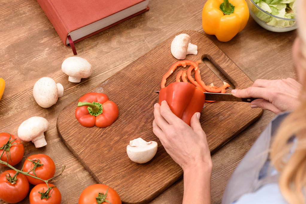 abgeschnittenes Bild einer Frau, die Paprika in der Küche schneidet - Foto, Bild