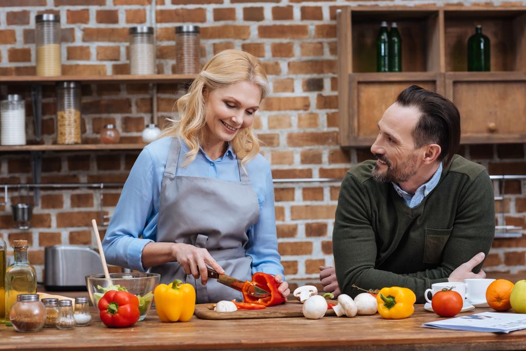 mari souriant regardant femme pendant qu'elle coupe des légumes
 - Photo, image
