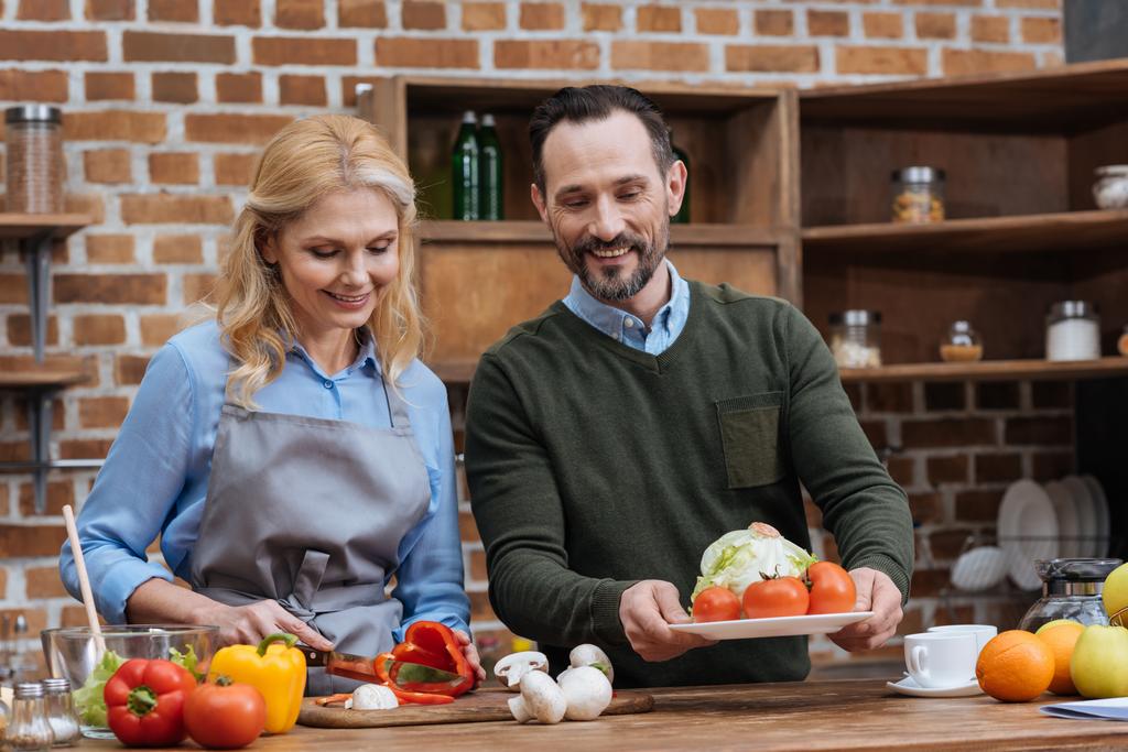 дружина ріже овочі і чоловік кладе тарілку на стіл
 - Фото, зображення