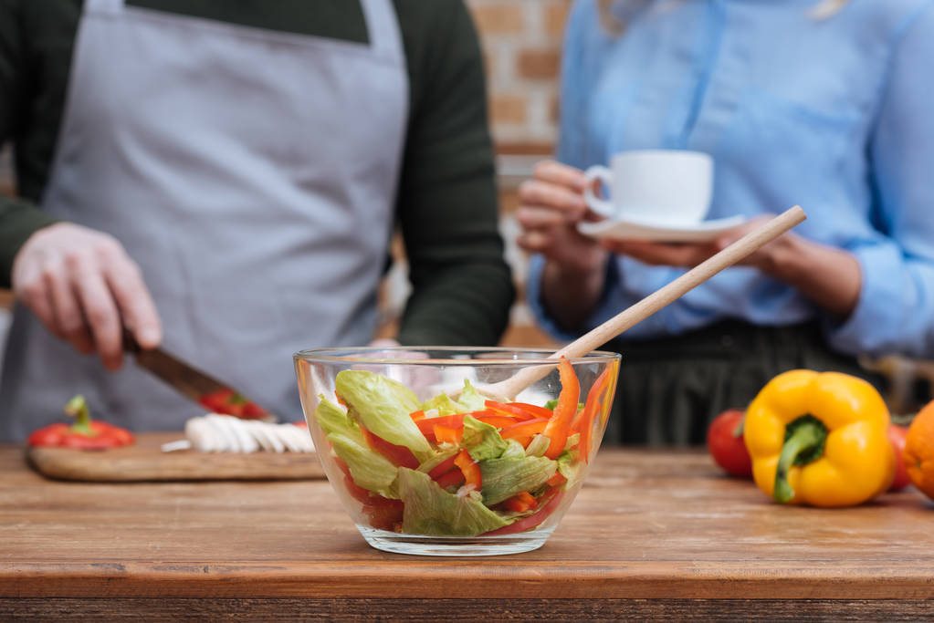 обрізане зображення пари, що готує їжу з салатом на передньому плані
 - Фото, зображення