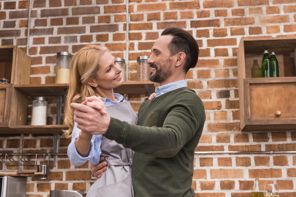 улыбающиеся жена и муж танцуют на кухне
 - Фото, изображение