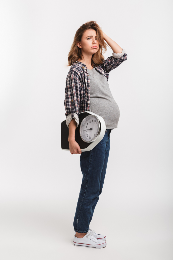naštvaná těhotná žena drží váhy a při pohledu na fotoaparát izolované na bílém  - Fotografie, Obrázek