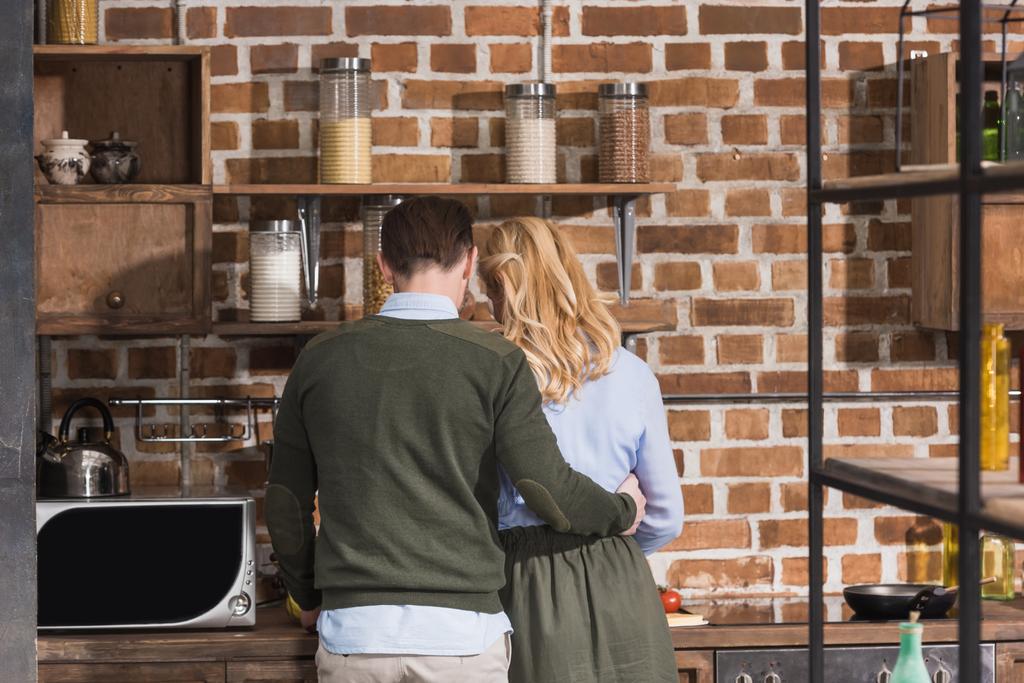 takana näkymä aviomies halaus vaimo keittiössä
 - Valokuva, kuva
