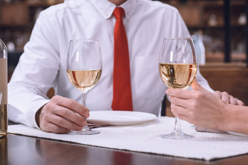 cropped image of couple holding hands and glasses of white wine at romantic dinner - Photo, Image