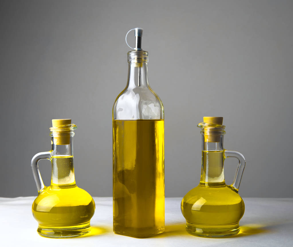 drei transparente Flaschen Olivenölglas mit Korken auf weißem Tisch in der Küche  - Foto, Bild