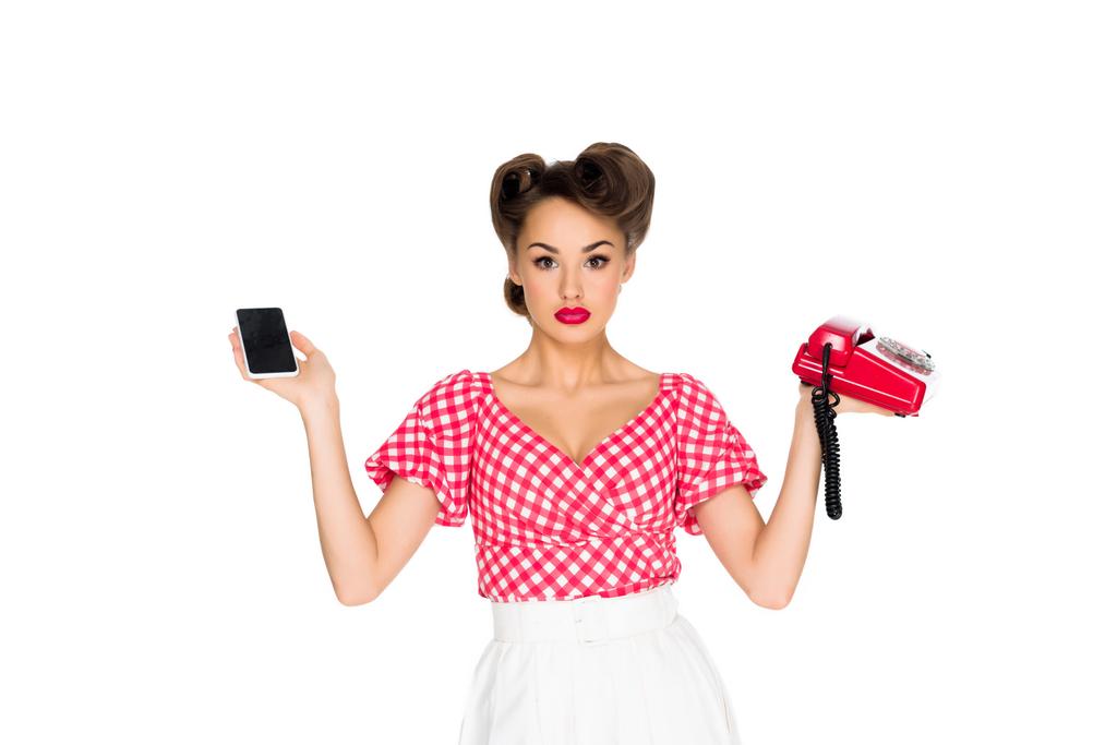 Porträt einer stilvollen Frau in Retro-Kleidung, die Smartphone und altes Telefon isoliert auf Weiß hält - Foto, Bild