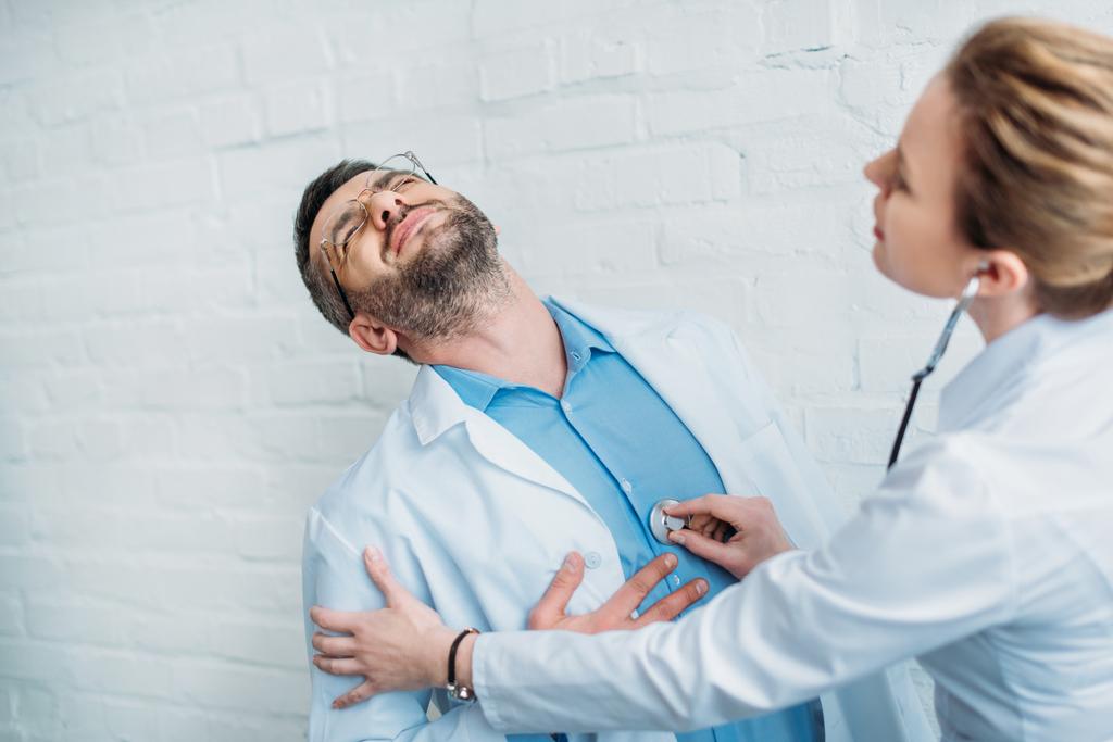 lekarka słuchając bicia serca kolegi, który ma atak serca z stetoskop - Zdjęcie, obraz