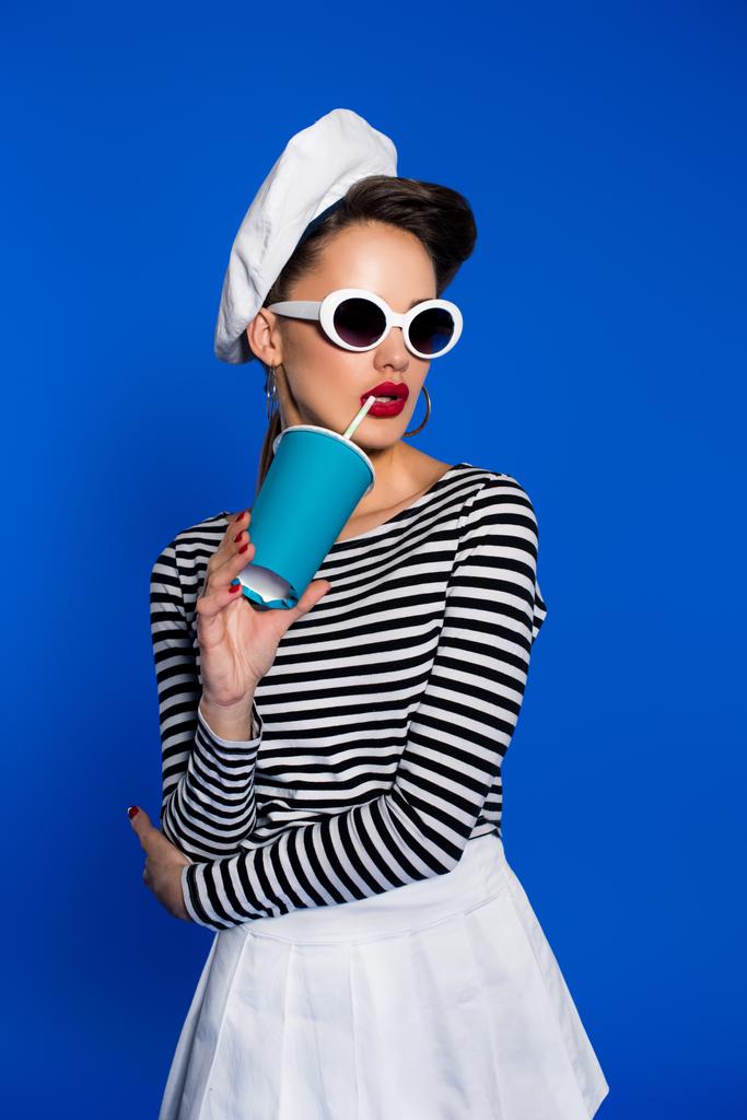 Portret van stijlvolle jongedame met drank in papier beker geïsoleerd op blauw - Foto, afbeelding