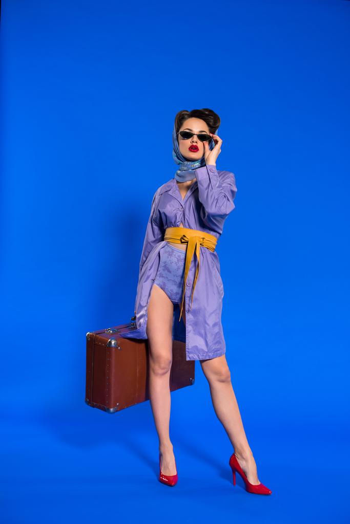 модна молода жінка в ретро одязі з валізою ізольована на синьому
 - Фото, зображення
