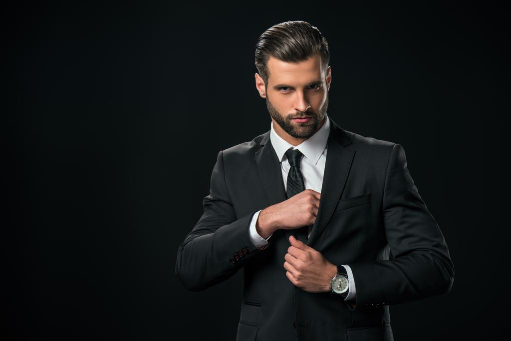 handsome businessman taking something from pocket of jacket, isolated on black - Photo, Image