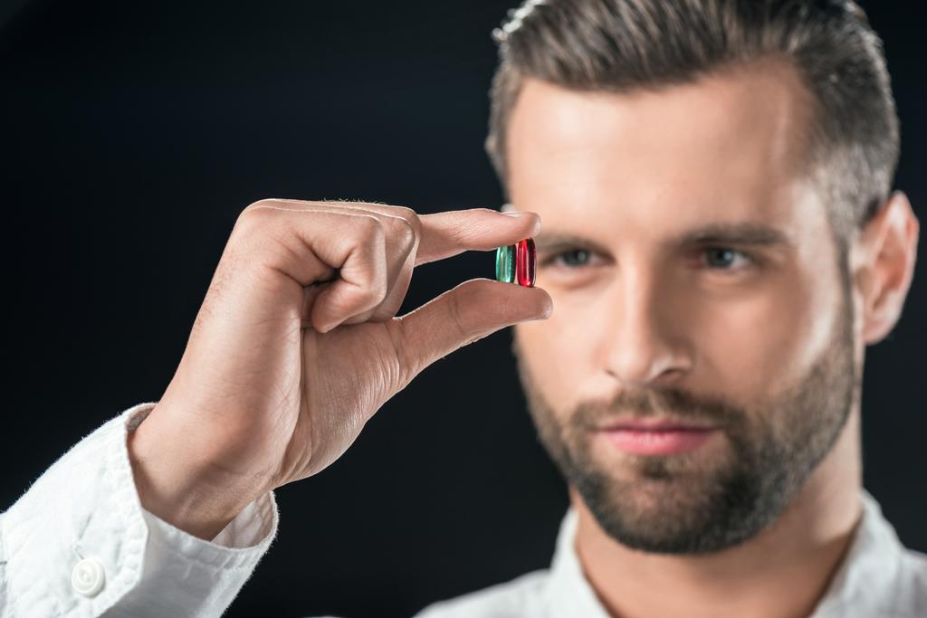 handsome businessman looking at blue and red pills, isolated on black - Photo, Image