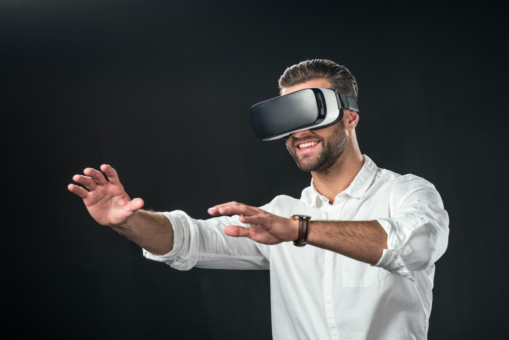 usmívající se muž používající soupravu pro virtuální realitu, izolované na černém pozadí - Fotografie, Obrázek