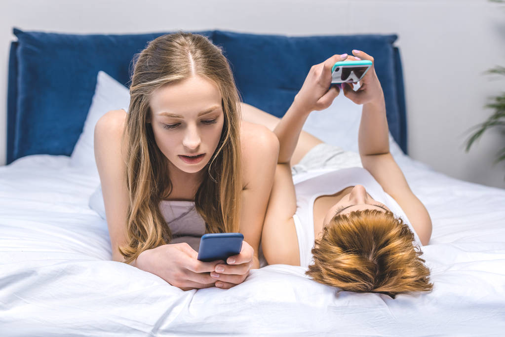 jovem casal lésbico networking com smartphones na cama
 - Foto, Imagem