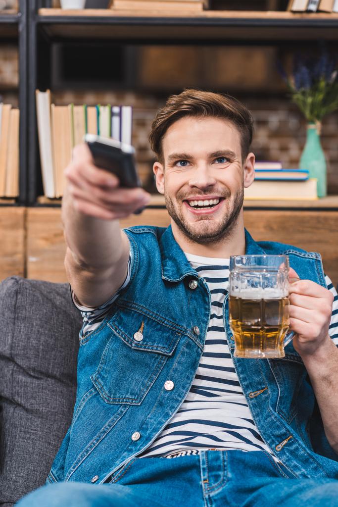 χαρούμενος νεαρός άνδρας κρατά ποτήρι μπύρας και μακρινός ελεγκτής - Φωτογραφία, εικόνα