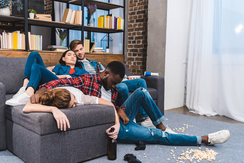 junge multiethnische Freunde schlafen in chaotischem Zimmer mit Popcorn und Bierflaschen - Foto, Bild