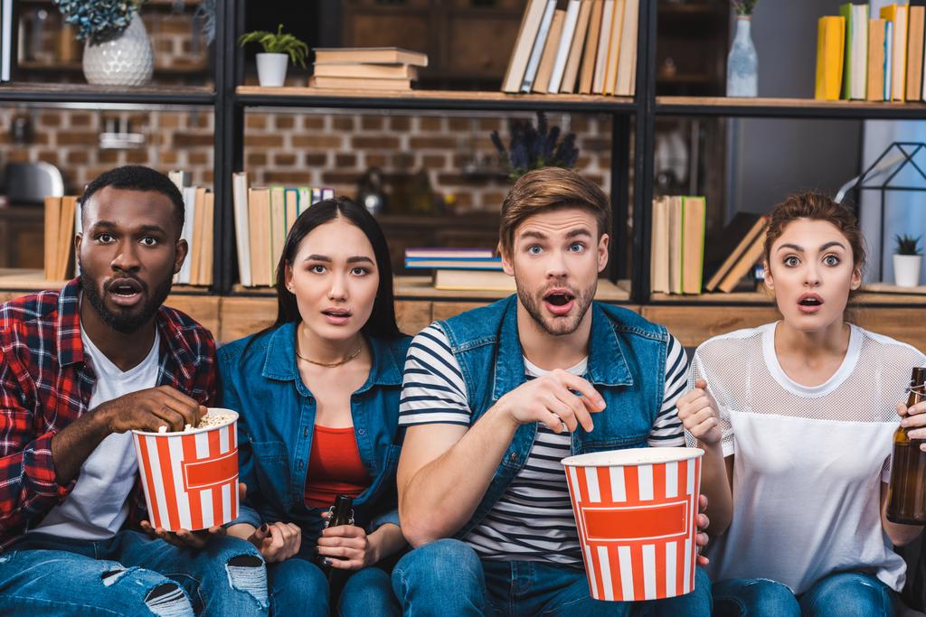 döbbenve fiatal többnemzetiségű meg pattogatott kukoricát eszik, és iszik sört, tv nézés közben - Fotó, kép