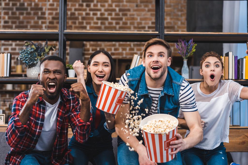 emotional young multiethnic friends eating popcorn and watching tv - Photo, Image