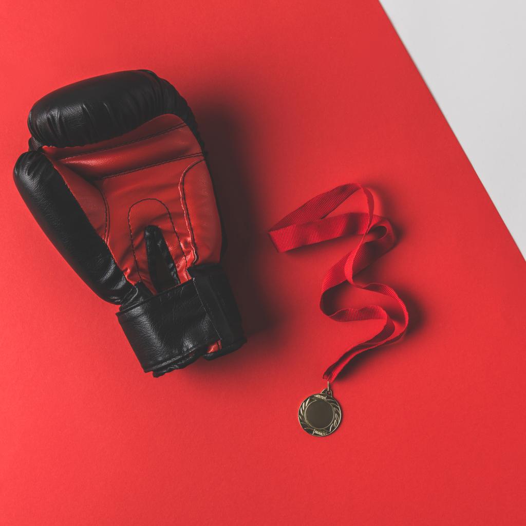 Ansicht von Boxhandschuh mit Medaille auf roter Oberfläche - Foto, Bild
