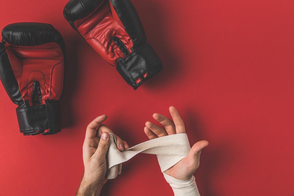 bijgesneden schot van bokser handen in elastische bandage voor strijd op rode oppervlak bedekken - Foto, afbeelding