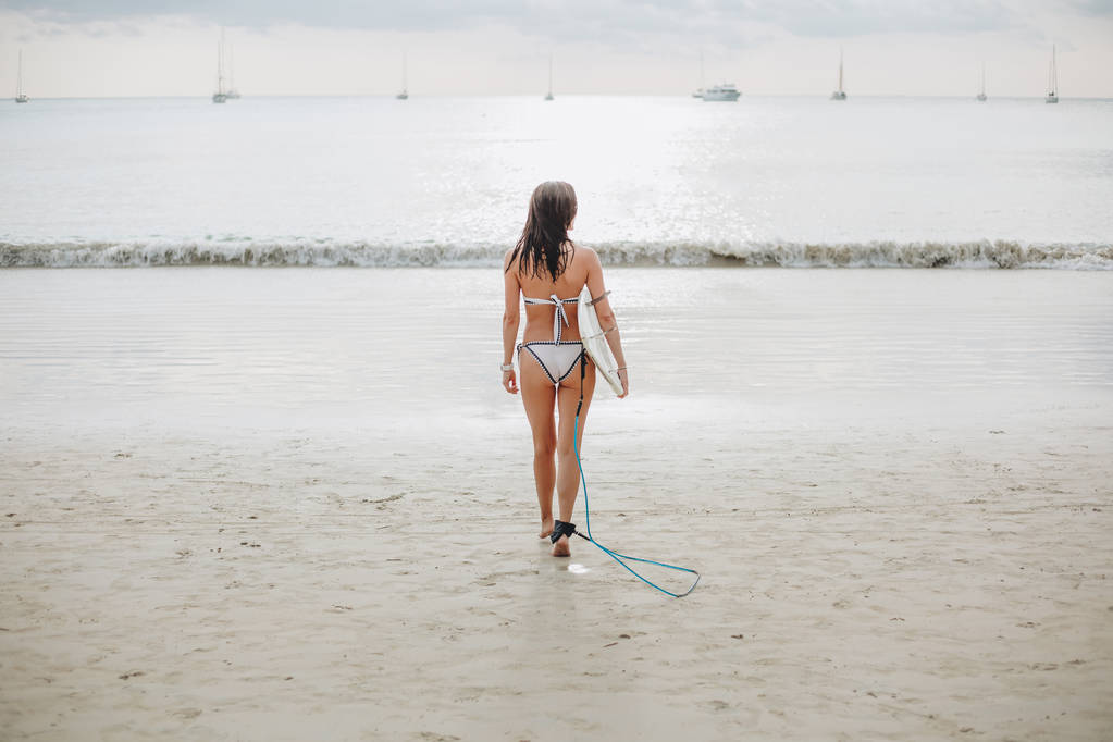 vue arrière de la fille en maillot de bain marchant avec planche de surf sur la plage en mer
 - Photo, image