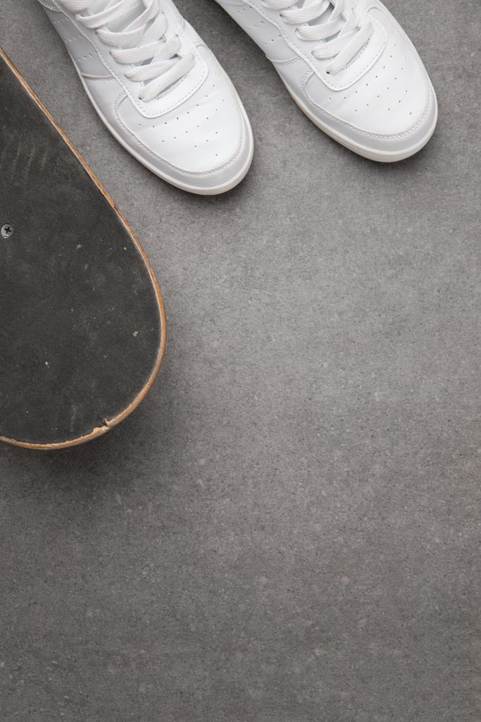 κάτοψη του Λευκά αθλητικά παπούτσια και skateboard στην γκρίζα άσφαλτο επιφάνεια - Φωτογραφία, εικόνα