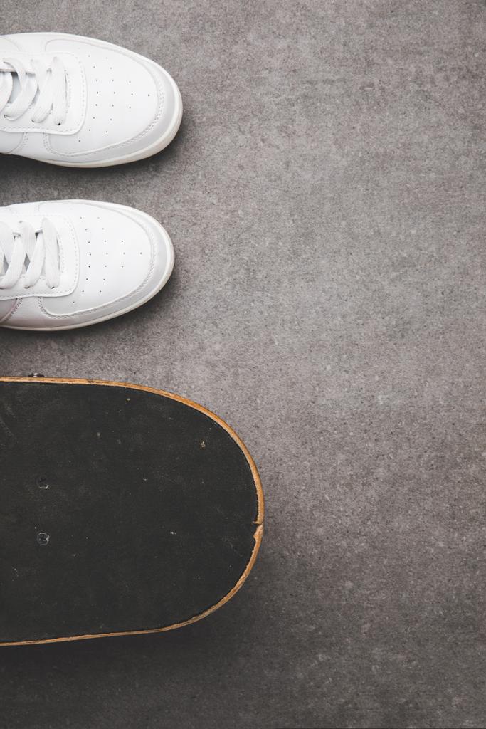 вид зверху на білі кросівки та скейтборд на бетонній поверхні
 - Фото, зображення