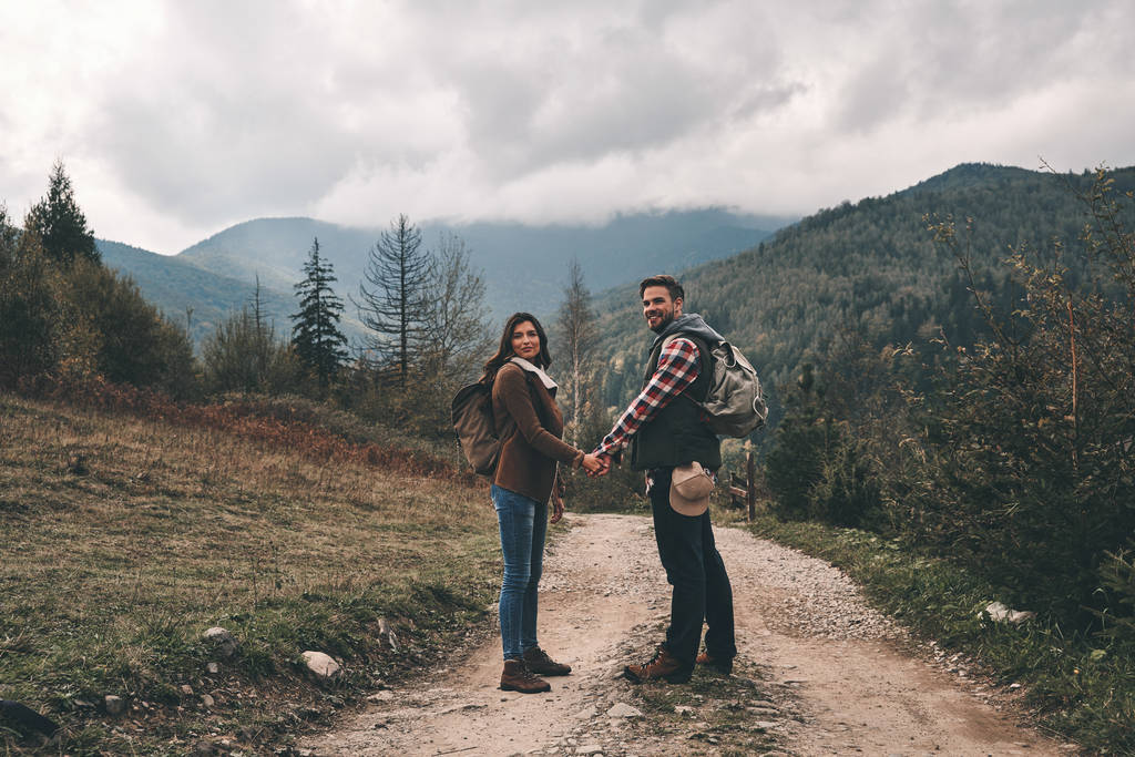 バックパック山の道の上に立って、手を繋いでいるカップルします。  - 写真・画像
