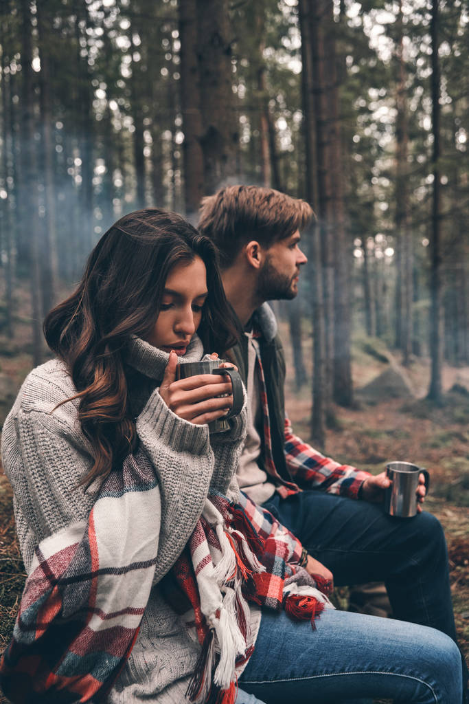 Beau jeune couple tenant des tasses avec des boissons chaudes dans la forêt
 - Photo, image