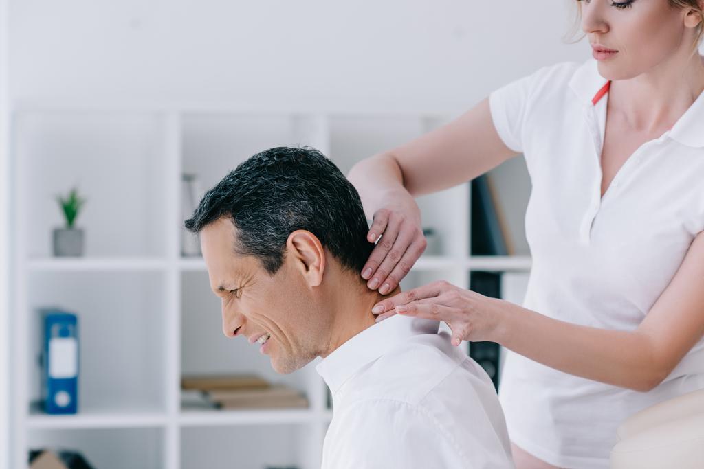 vista lateral de masajista haciendo masaje de cuello sentado para el cliente en la oficina
 - Foto, imagen