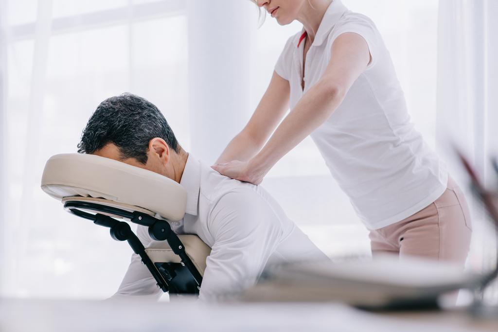 masajista haciendo masaje de espalda sentado para hombre de negocios en la oficina
 - Foto, Imagen