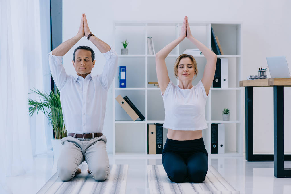 Reifer Geschäftsmann meditiert im Büro mit seinem Trainer auf Yogamatten - Foto, Bild