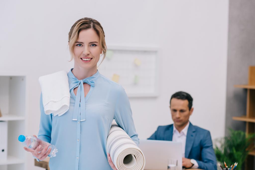 donna d'affari con attrezzature per il fitness in piedi in ufficio moderno mentre il suo collega lavora con il computer
 - Foto, immagini