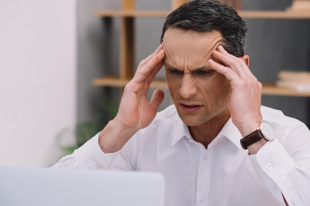 rijpe zakenman met pijnlijke migraine proberen te werken op kantoor - Foto, afbeelding